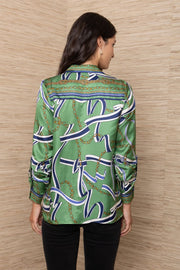 A woman modeling a green silk button-up shirt with an abstract blue, white, and gold chain pattern.