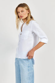 Side view of a woman wearing a white tencel shirt and light blue jeans on a plain background