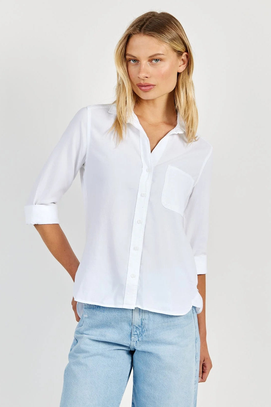 Front view of a woman wearing a white tencel shirt and light blue jeans on a plain background