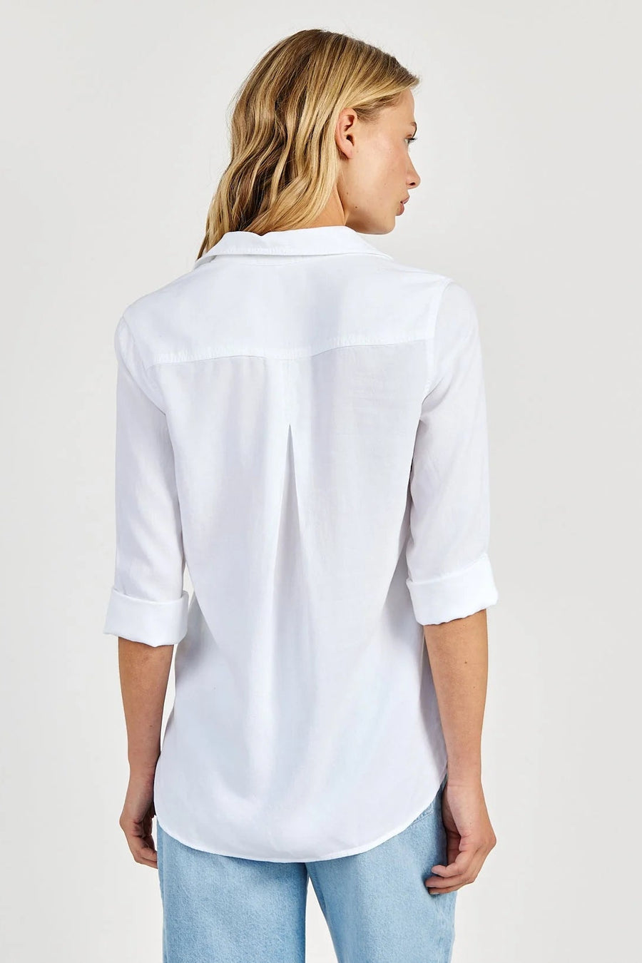 Back view of a woman wearing a white tencel shirt and light blue jeans on a plain background