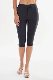 A model wearing dark charcoal gray capri pants and white heeled sandals, shown from the waist down against a plain white studio background.