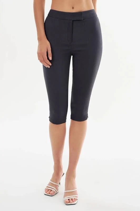 A model wearing dark charcoal gray capri pants and white heeled sandals, shown from the waist down against a plain white studio background.