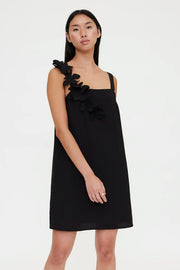 Woman wearing a black sleeveless mini dress with floral appliqué detailing on one shoulder, front