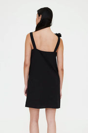 Woman wearing a black sleeveless mini dress with floral appliqué detailing on one shoulder, back