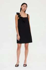 Woman wearing a black sleeveless mini dress with floral appliqué detailing on one shoulder, front