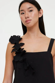 Woman wearing a black sleeveless mini dress with floral appliqué detailing on one shoulder, detail