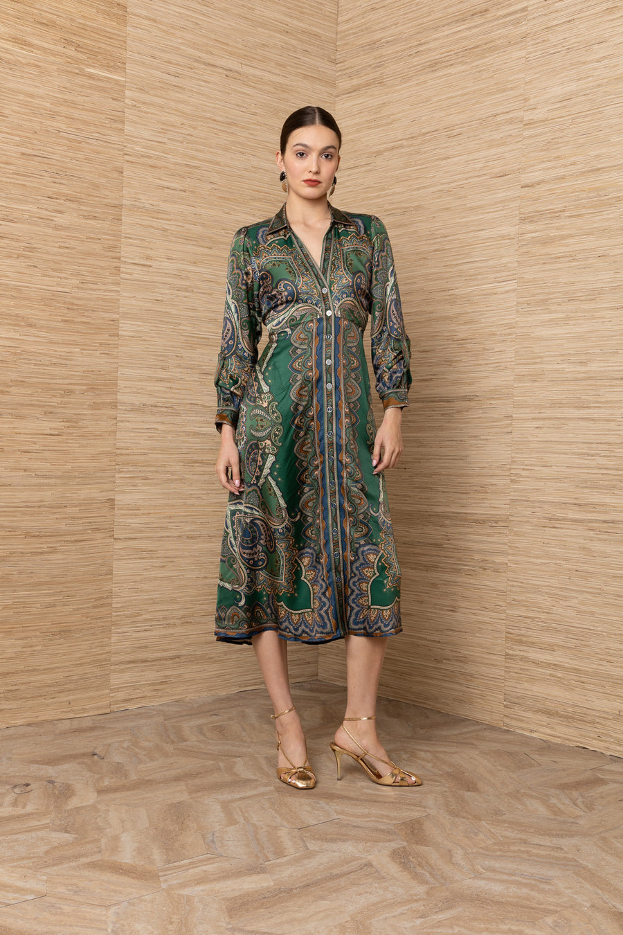 A woman models a green long-sleeve midi shirt dress with a detailed paisley and floral pattern in blue, gold, and beige.