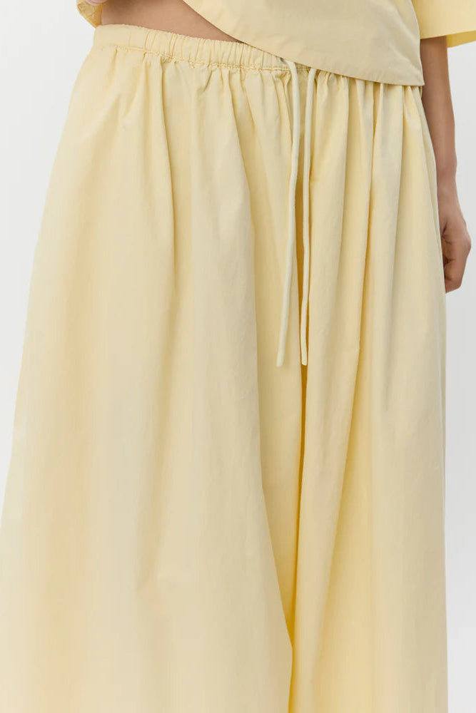 Woman wearing a pale yellow elastic-waist midi skirt with a drawstring, detail