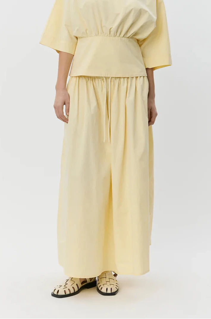 Woman wearing a pale yellow elastic-waist midi skirt with a drawstring, front