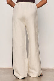 Woman wearing lightweight sand-colored wide-leg pants with contrasting black side stripe detailing. Features a comfortable pull-on elastic waistband, relaxed fit through the leg, and a fluid full-length silhouette. Designed with side pockets and a soft drape for effortless everyday wear, back