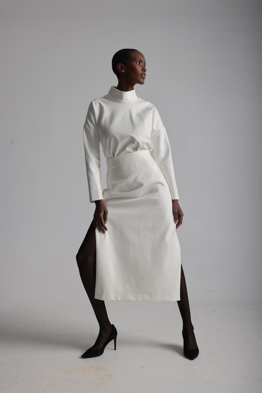 Woman wearing a white outfit with a high collar and skirt on a plain background