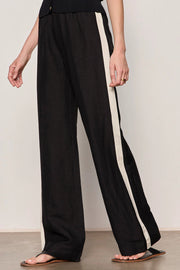 Woman wearing black lightweight  wide-leg pants with contrasting black side stripe detailing. Features a comfortable pull-on elastic waistband, relaxed fit through the leg, and a fluid full-length silhouette. Designed with side pockets and a soft drape for effortless everyday wear, side