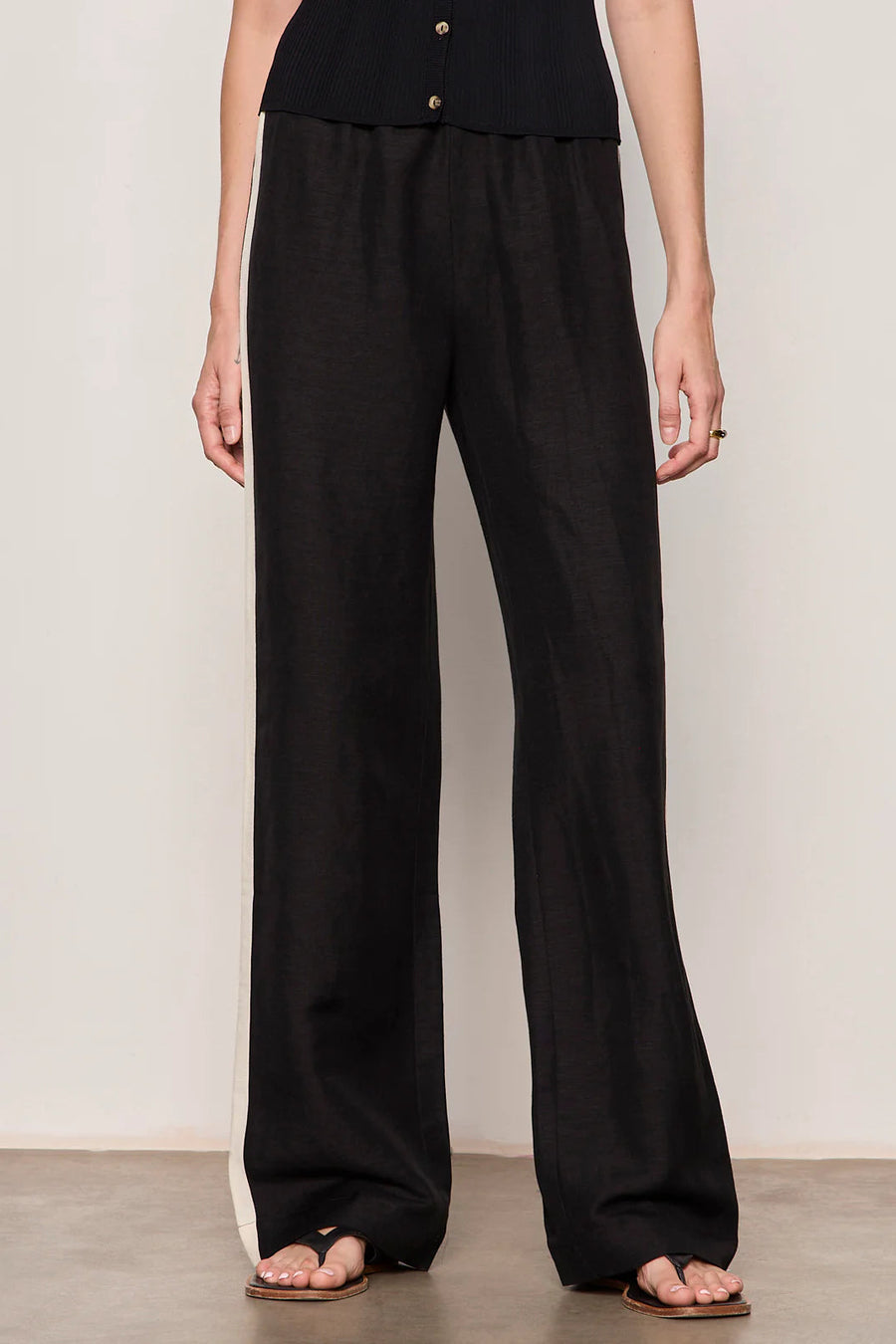 Woman wearing black lightweight  wide-leg pants with contrasting black side stripe detailing. Features a comfortable pull-on elastic waistband, relaxed fit through the leg, and a fluid full-length silhouette. Designed with side pockets and a soft drape for effortless everyday wear, front