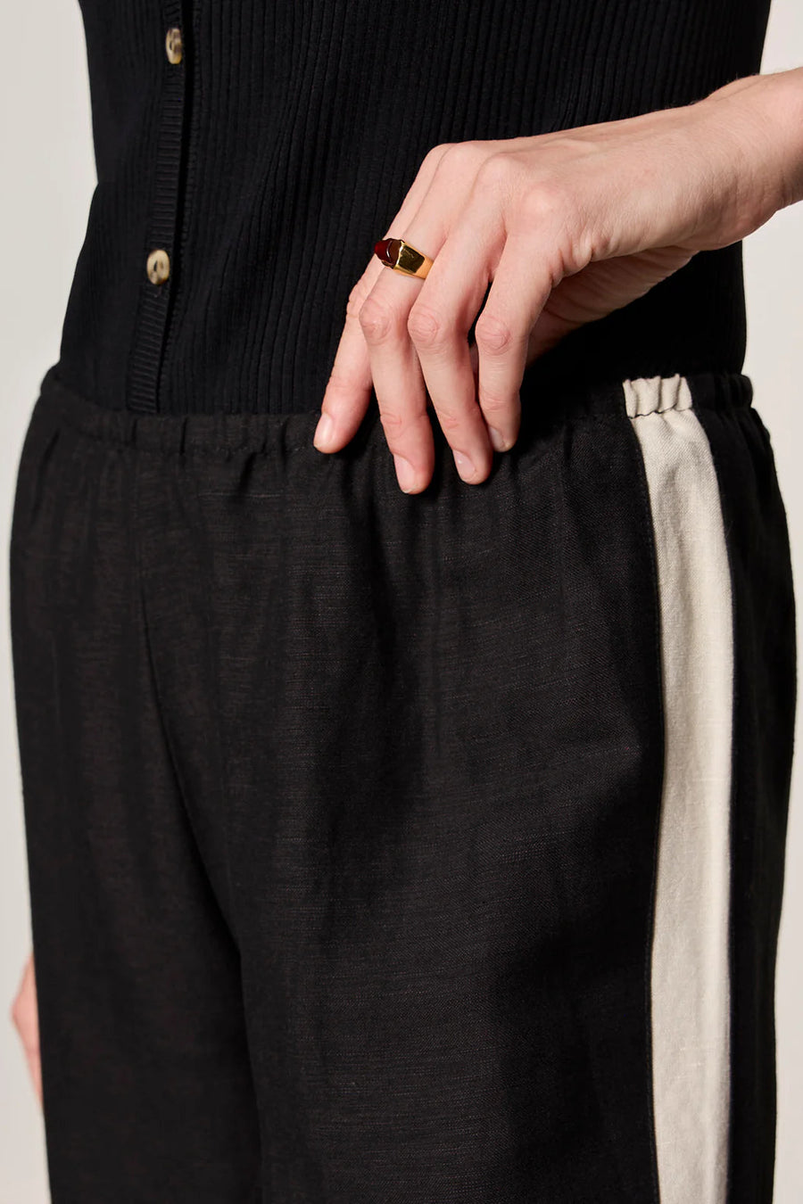 Woman wearing black lightweight  wide-leg pants with contrasting black side stripe detailing. Features a comfortable pull-on elastic waistband, relaxed fit through the leg, and a fluid full-length silhouette. Designed with side pockets and a soft drape for effortless everyday wear, closeup