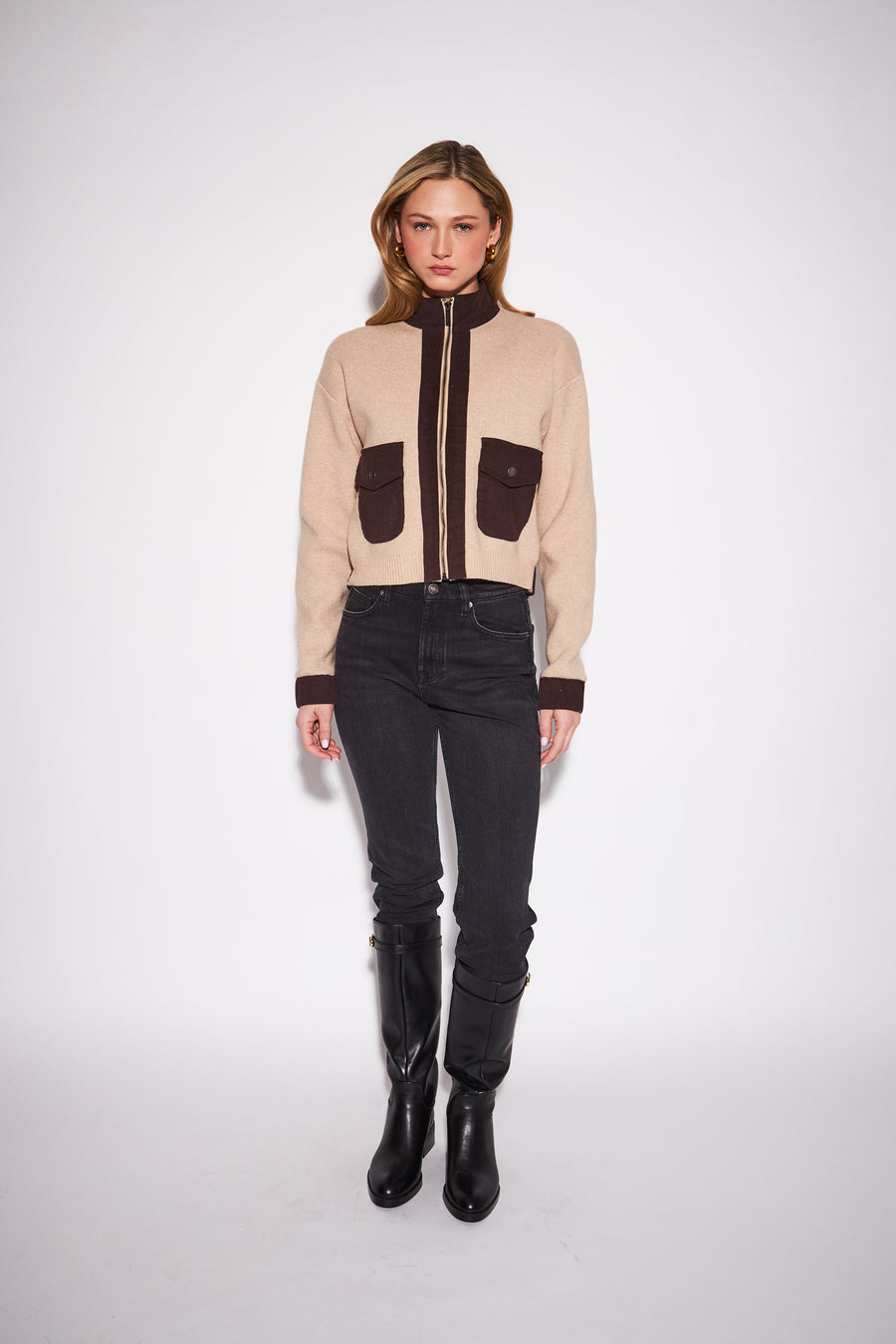 model wearing a cream cable knit zip up jacket with dark brown contrast trim and patch pockets