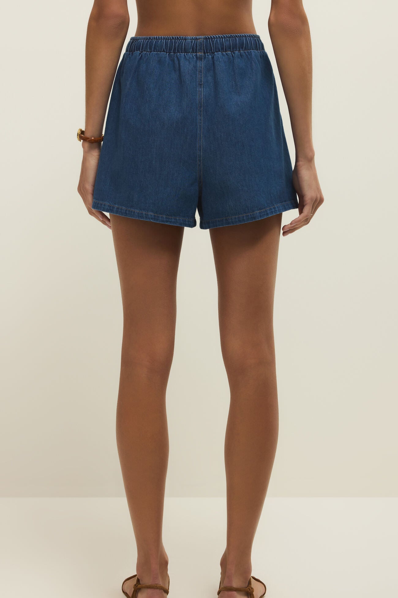 Woman wearing denim shorts in a dark blue wash with a drawstring and pockets, back view