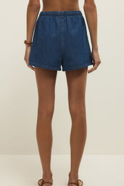 Woman wearing denim shorts in a dark blue wash with a drawstring and pockets, back view
