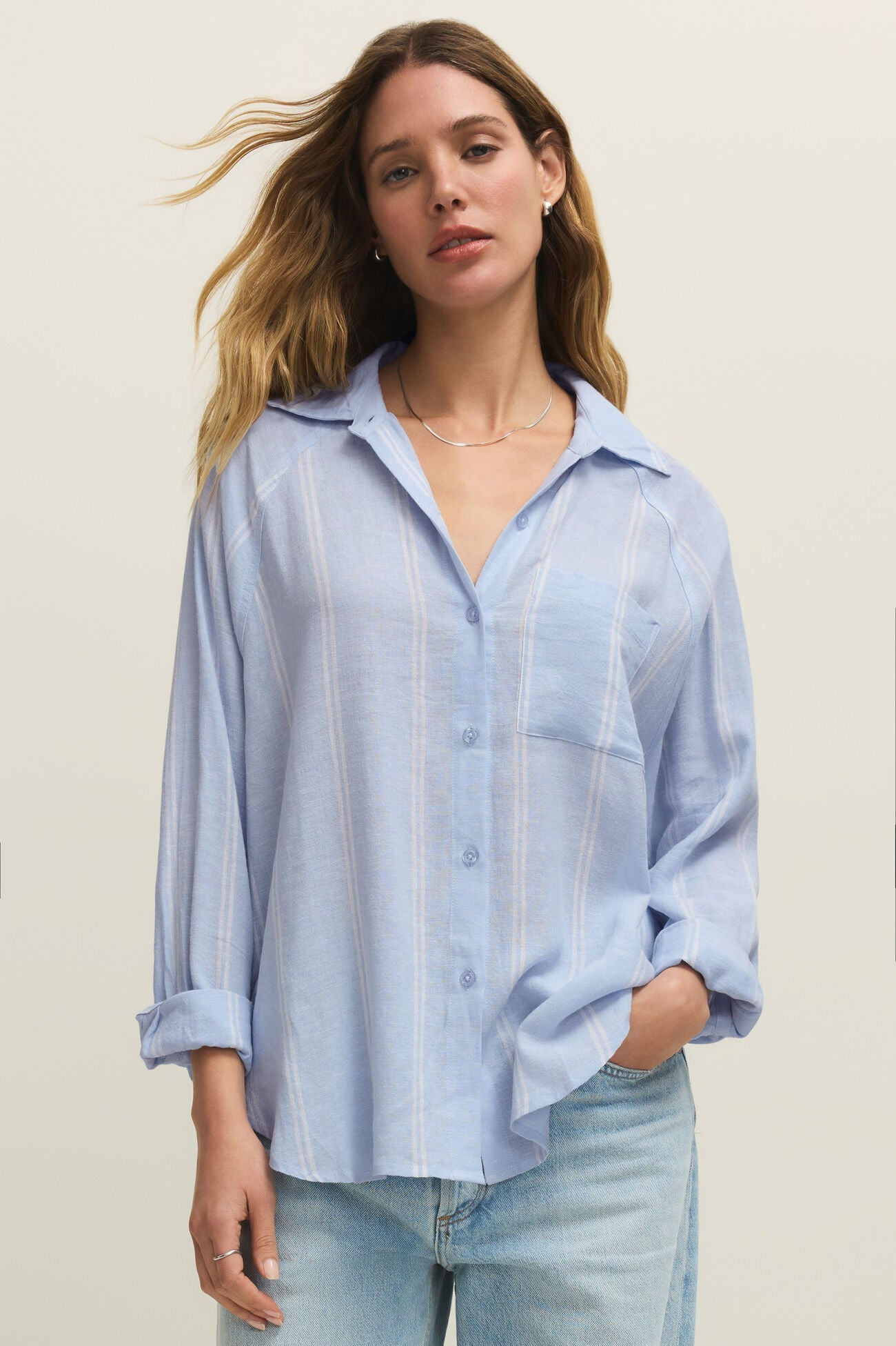 Woman wearing a oversized light blue long sleeve linen button down shirt with vertical white stripes, front view