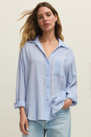 Woman wearing a oversized light blue long sleeve linen button down shirt with vertical white stripes, front view