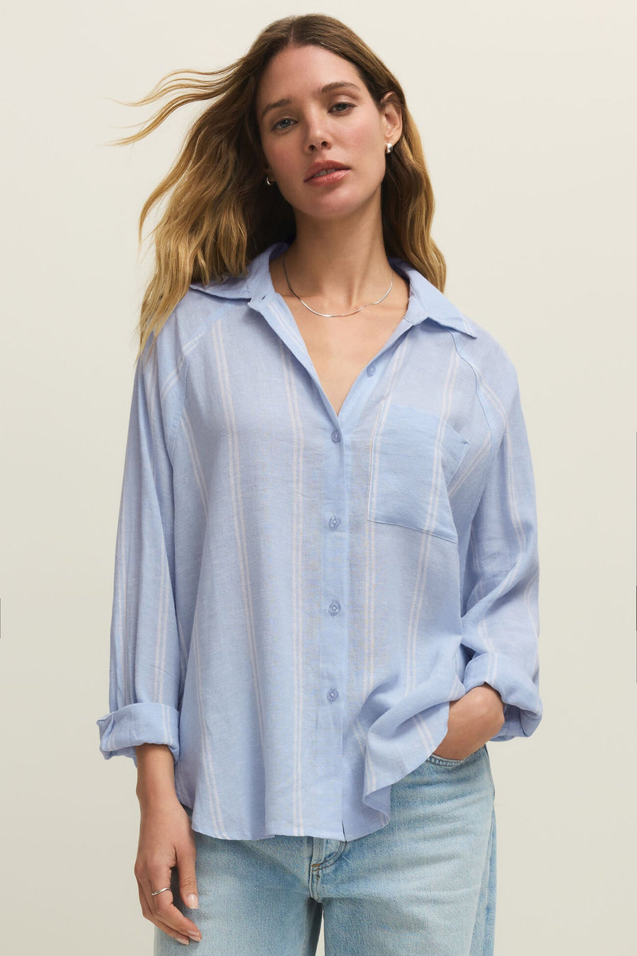 Woman wearing a oversized light blue long sleeve linen button down shirt with vertical white stripes, front view