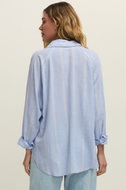 Woman wearing a oversized light blue long sleeve linen button down shirt with vertical white stripes, back view