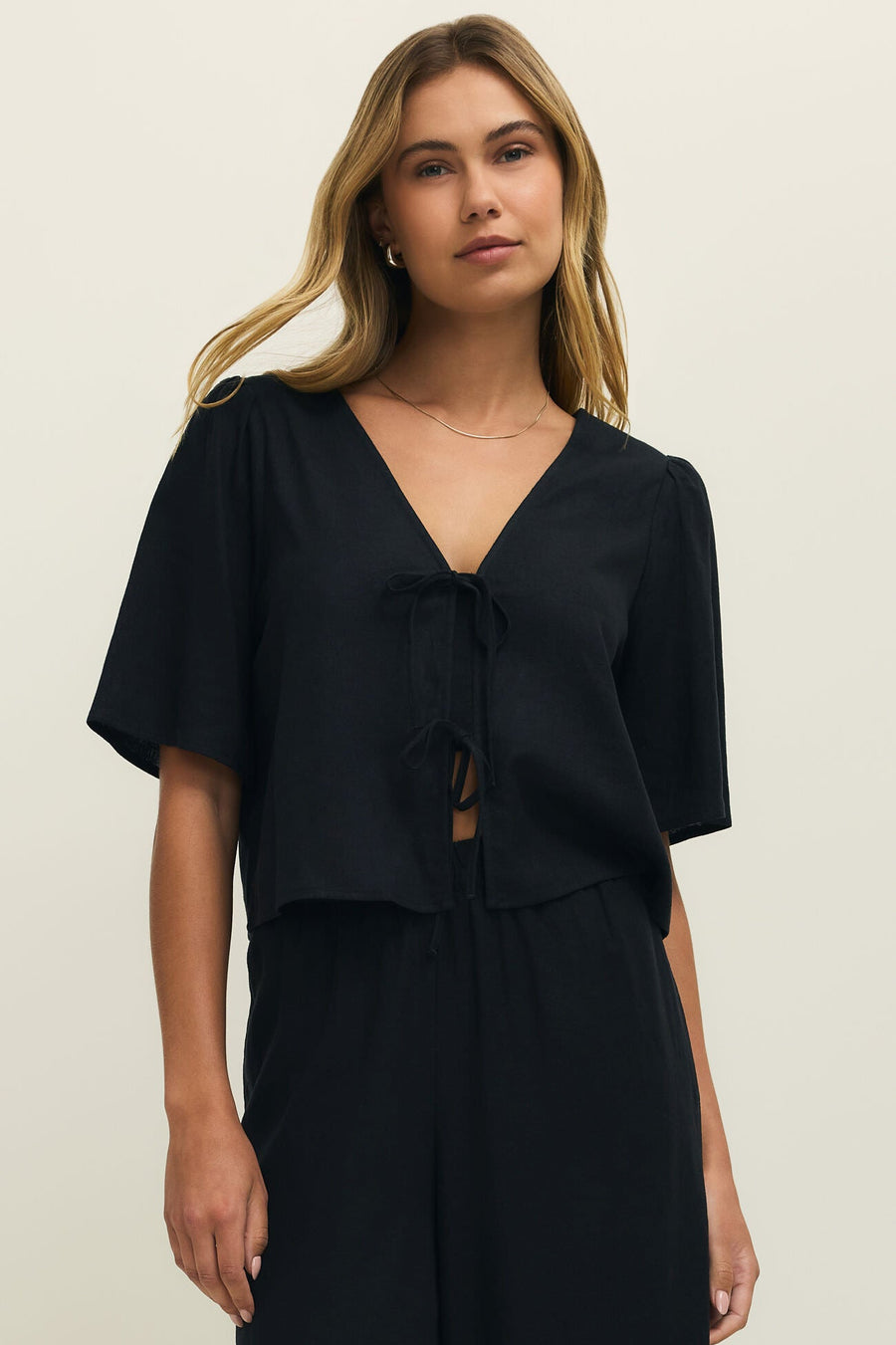 Woman wearing a black short sleeve linen top with two ties on the front, front view