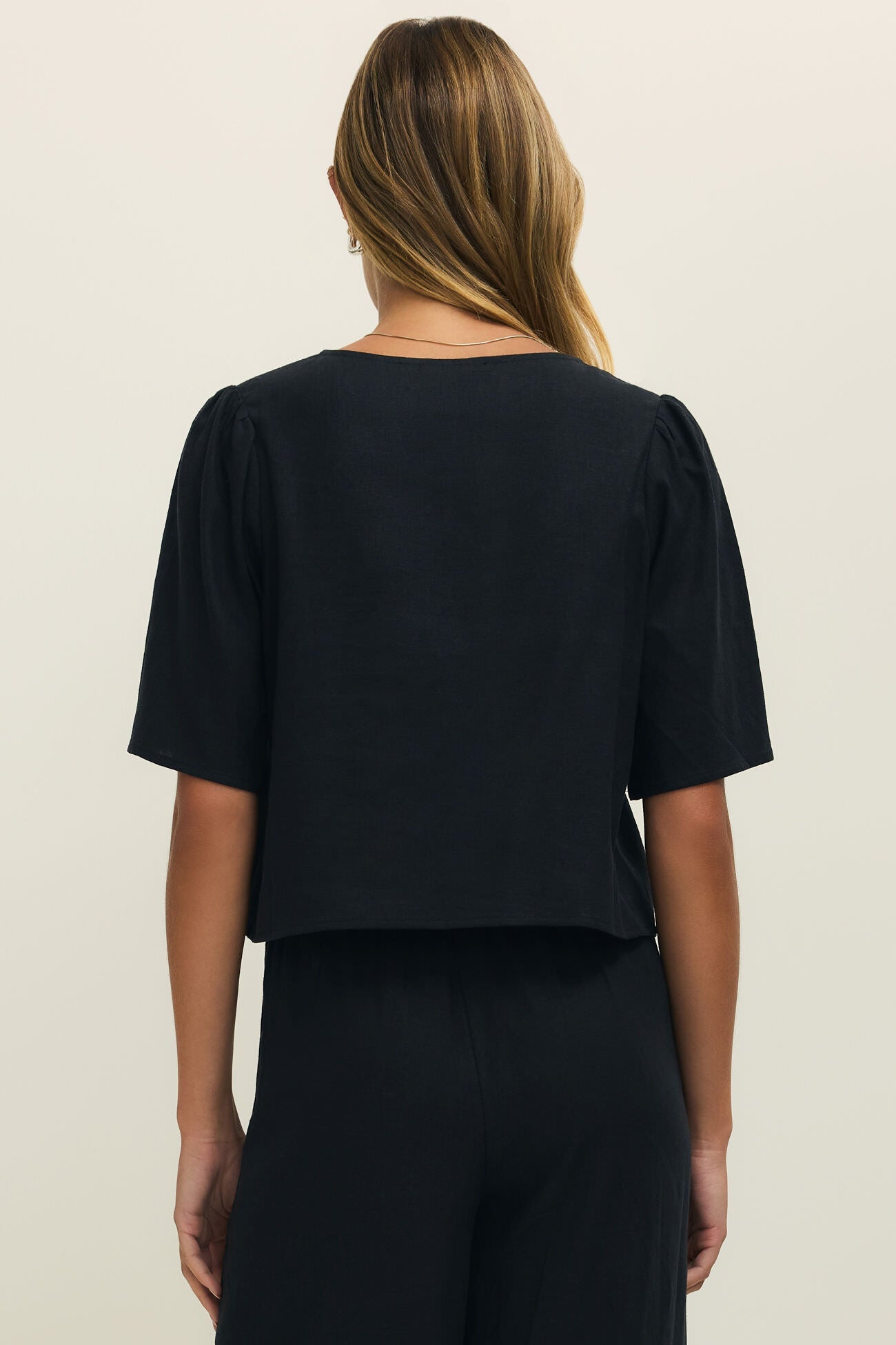Woman wearing a black short sleeve linen top with two ties on the front, back view