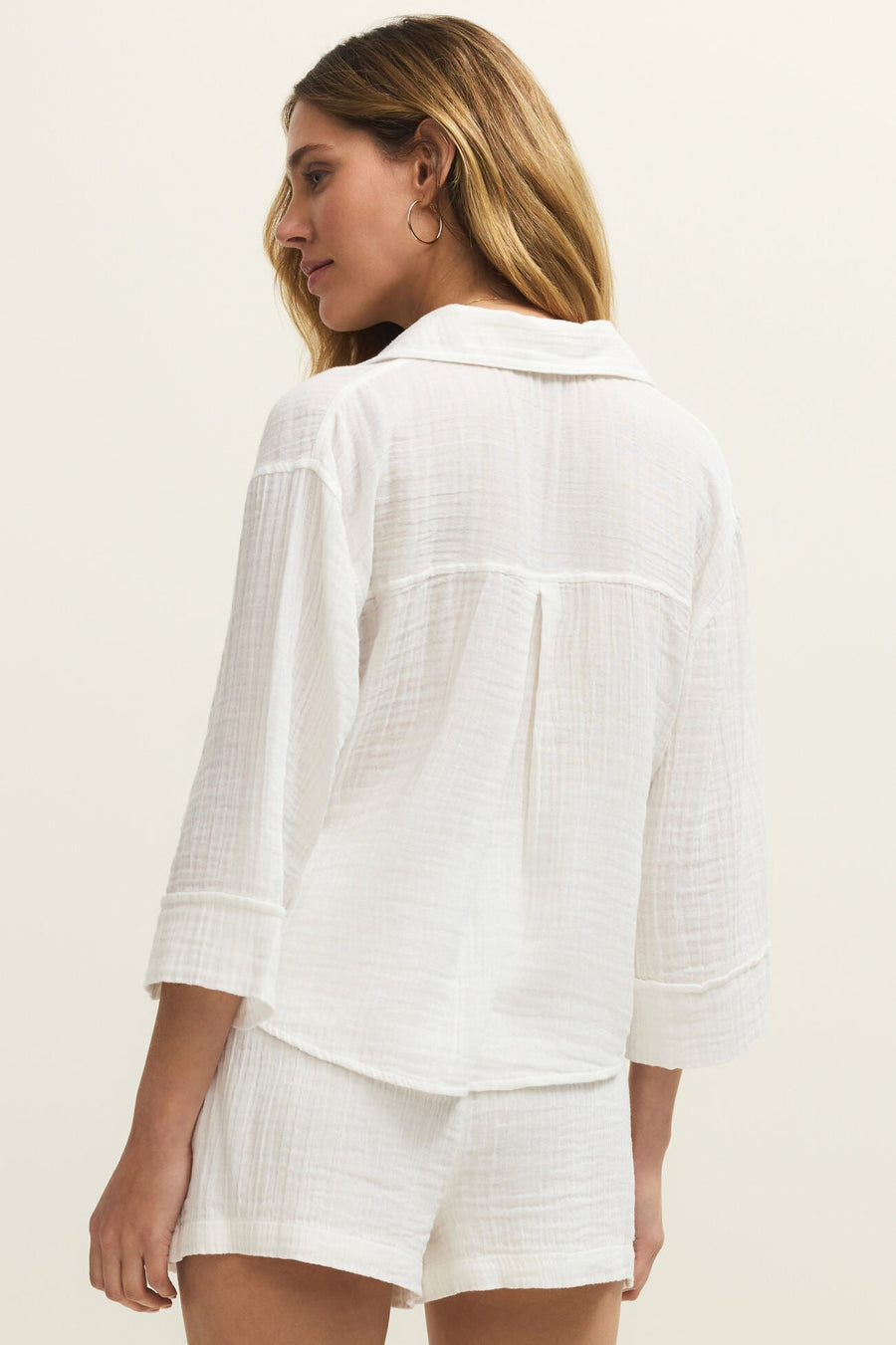 Woman wearing a white, relaxed fit button down shirt with two front pockets, back  view