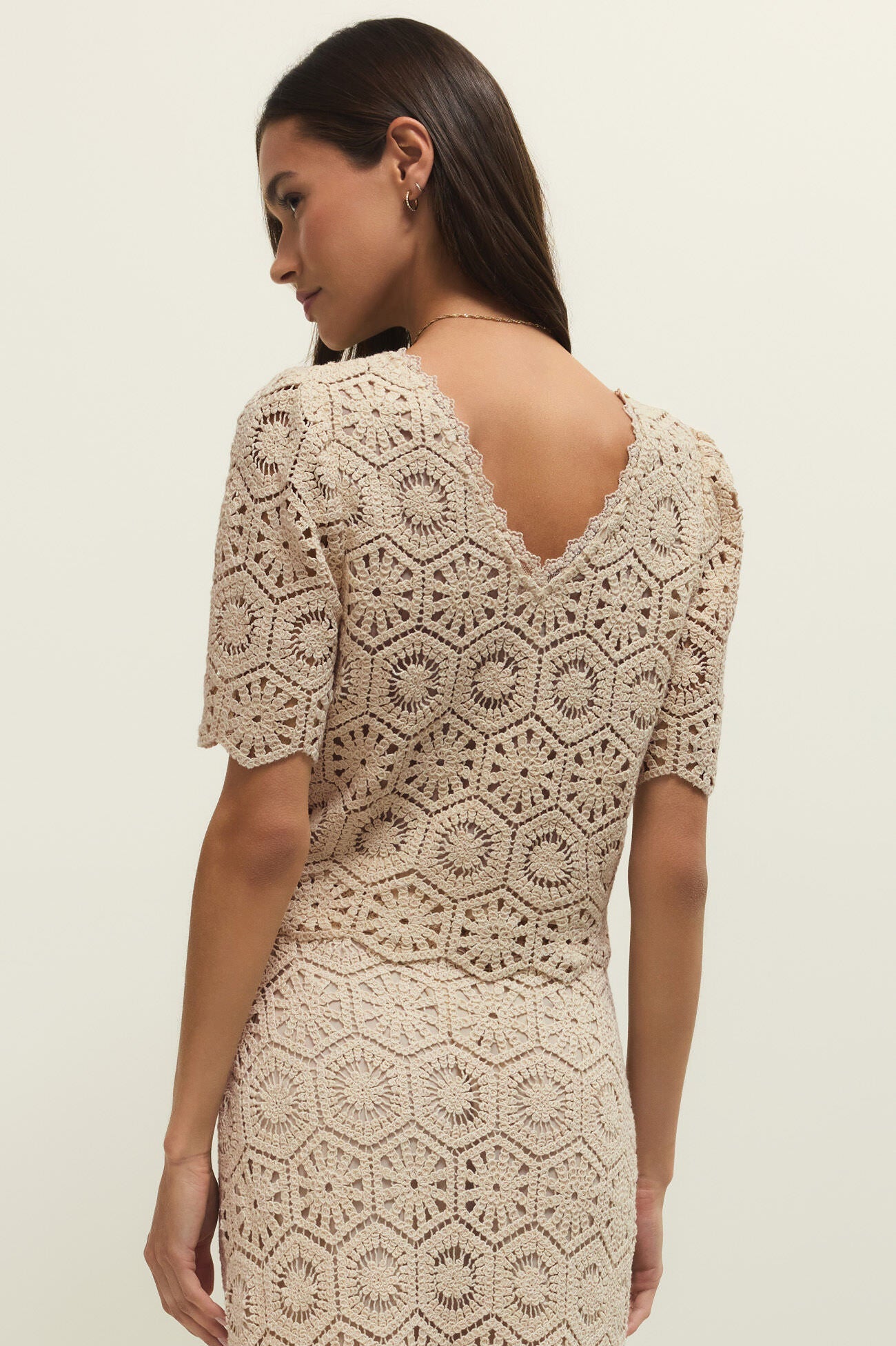 Woman wearing a beige crochet lace short sleeve top with scalloped hem, back view
