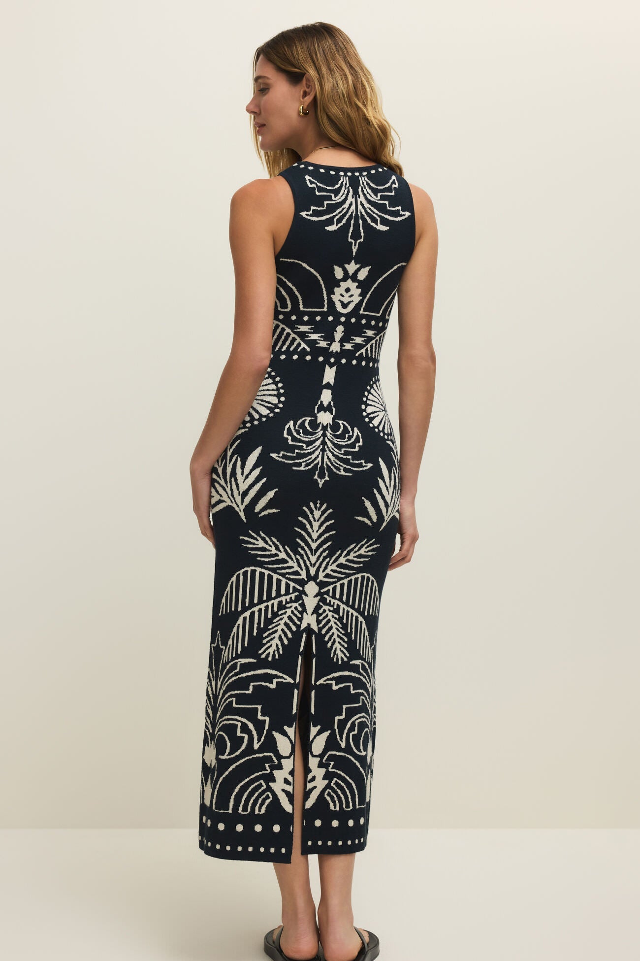 Woman wearing a long, dark blue sleeveless dress with a palm tree print, back view