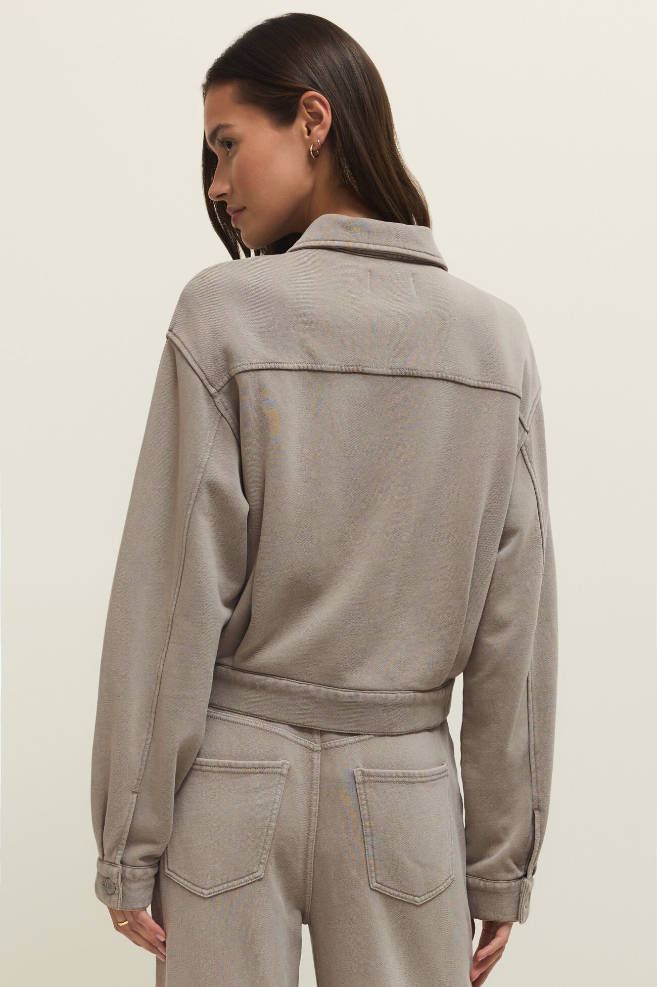 Woman wearing a taupe zip-front jacket with chest pockets, back view