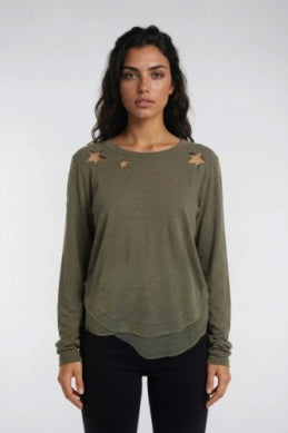 A woman modeling an olive green long-sleeve top with distressed star details on the shoulders, paired with black pants