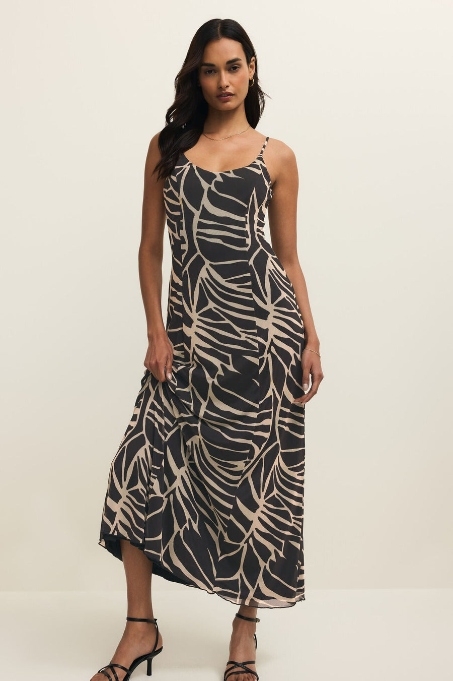 Woman wearing a long black dress with with a leaf print all over it, front view