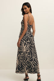 Woman wearing a long black dress with with a leaf print all over it, back view