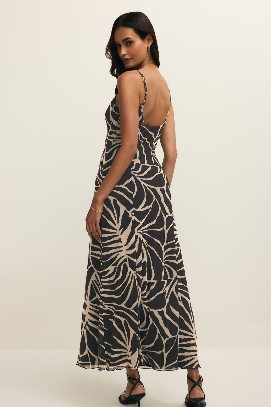 Woman wearing a long black dress with with a leaf print all over it, back view