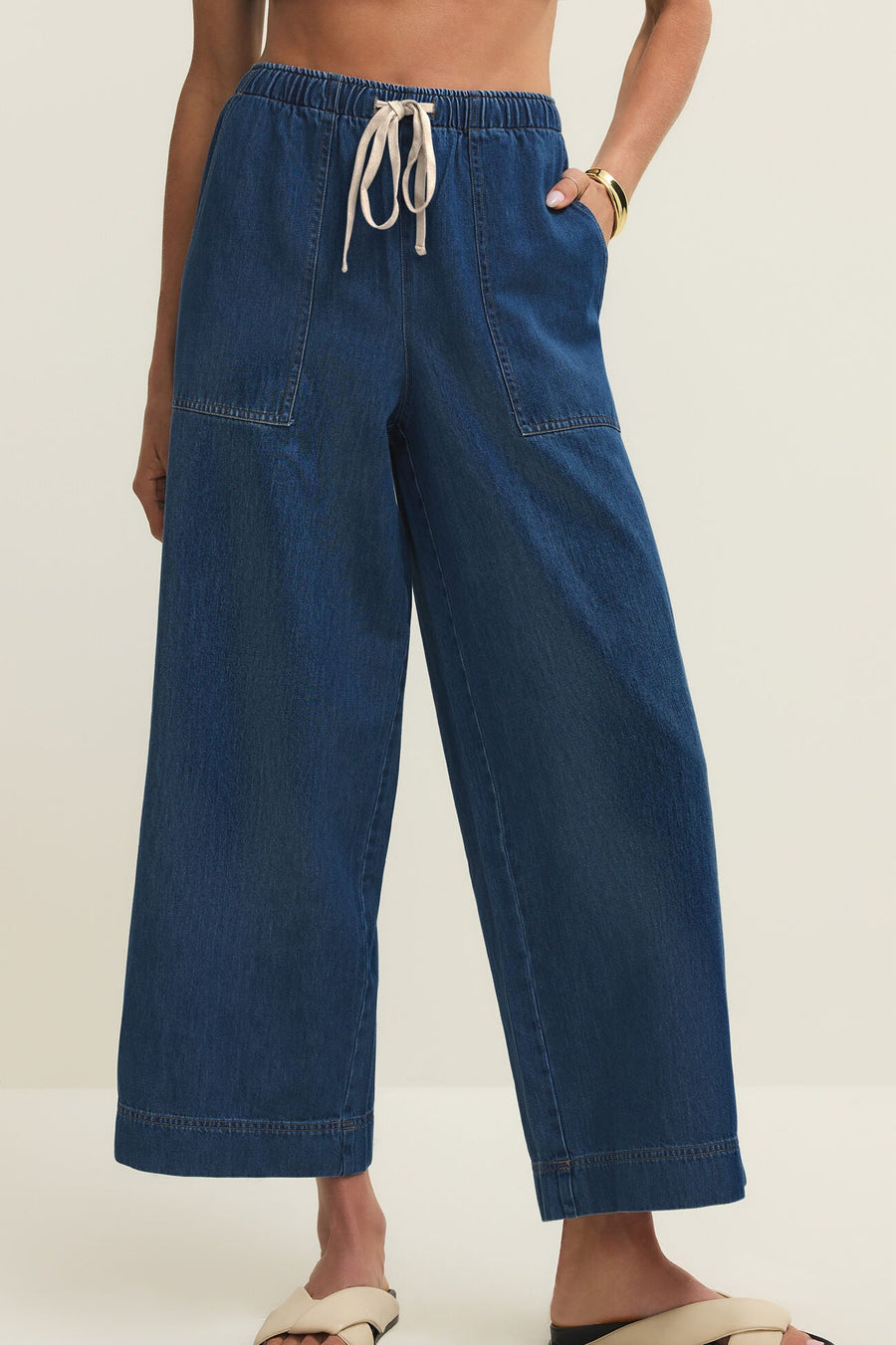 Woman wearing relaxed ankle length straight wide leg pants in a dark blue denim wash with a drawstring and pockets, front view