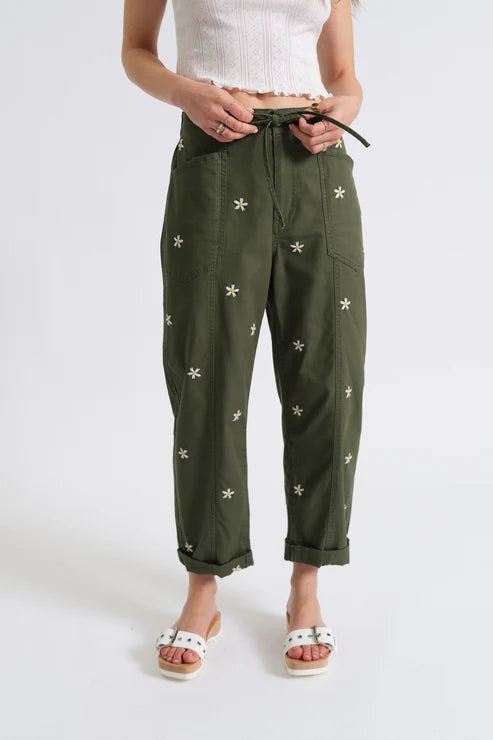 Woman wearing olive green drawstring pants embroidered with daisies, close up view