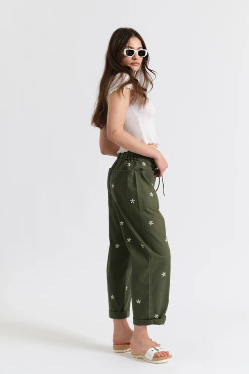Woman wearing olive green drawstring pants embroidered with daisies, side view