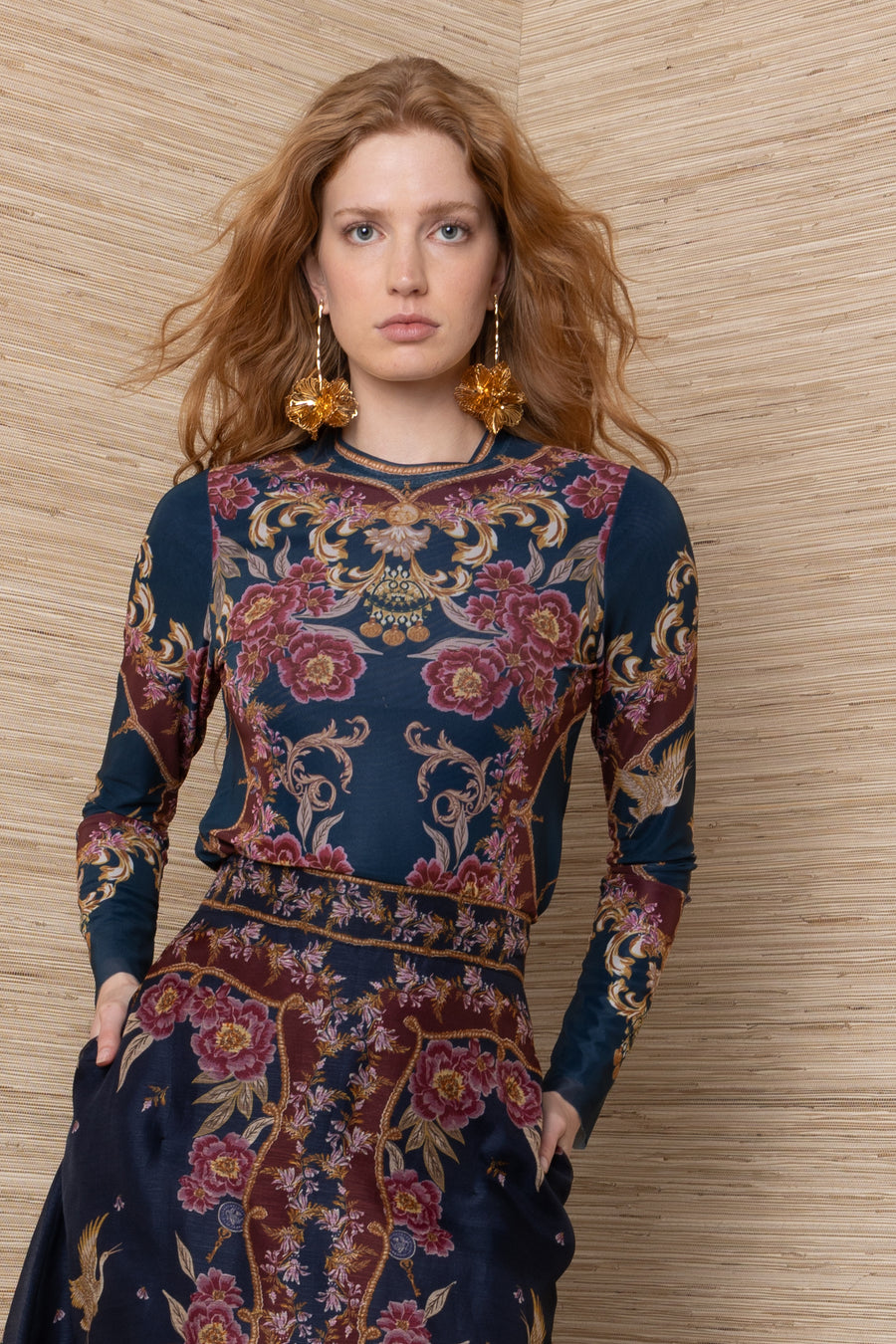 A woman modeling a long-sleeve navy blue dress with an intricate baroque-style floral and scroll pattern in burgundy, gold, and beige
