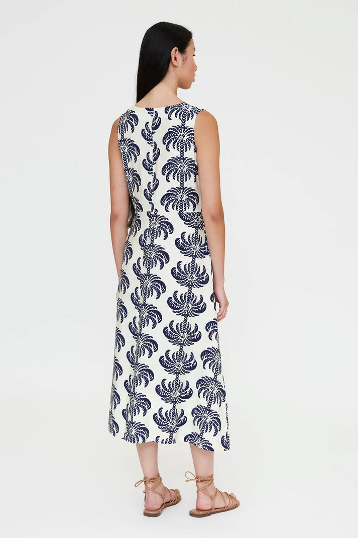 Woman wearing a sleeveless V-neck midi dress with a blue palm print and a tie waist, back view