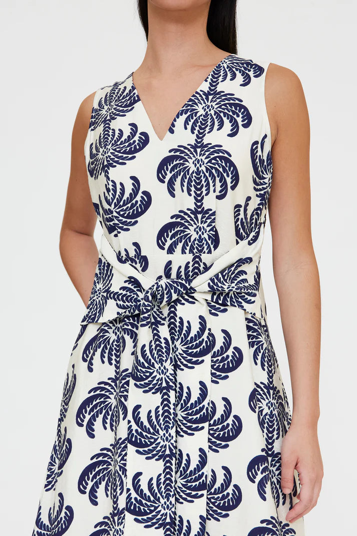 Woman wearing a sleeveless V-neck midi dress with a blue palm print and a tie waist, detail view