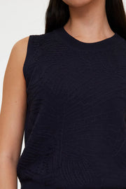 Woman wearing a navy sleeveless knit top with a crew neckline, detail view