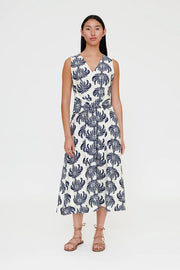 Woman wearing a sleeveless V-neck midi dress with a blue palm print and a tie waist, front view