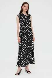 Woman wearing a black sleeveless midi dress with white polka dots and a wrap-style bodice, front