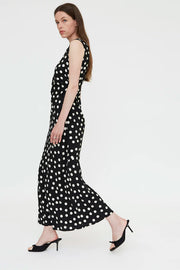 Woman wearing a black sleeveless midi dress with white polka dots and a wrap-style bodice, side