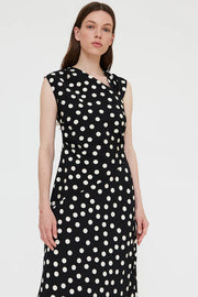 Woman wearing a black sleeveless midi dress with white polka dots and a wrap-style bodice, front