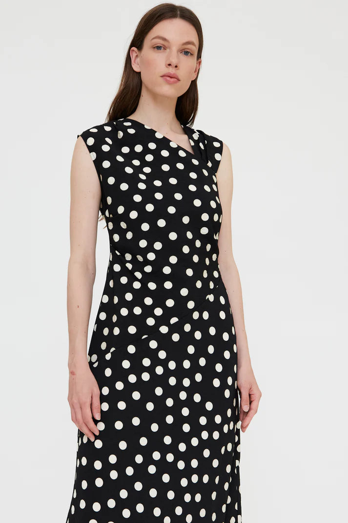 Woman wearing a black sleeveless midi dress with white polka dots and a wrap-style bodice, front