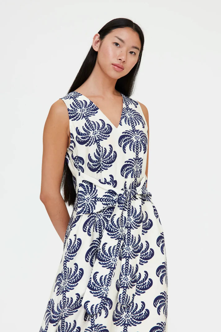 Woman wearing a sleeveless V-neck midi dress with a blue palm print and a tie waist