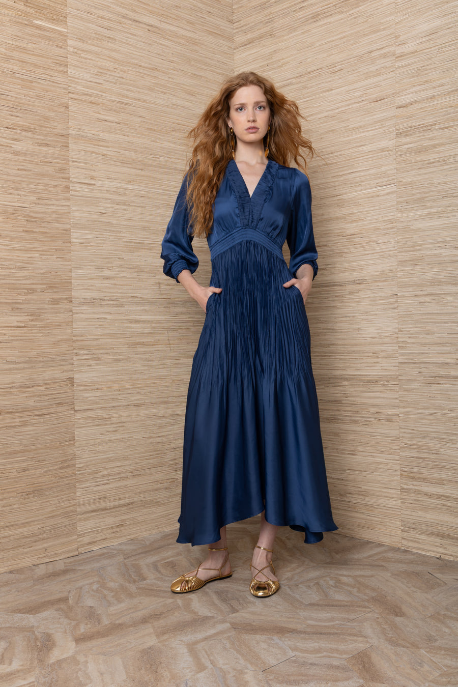 woman wearing a satin blue v neck long sleeve midi dress with ruching in the middle and cuffed sleeves