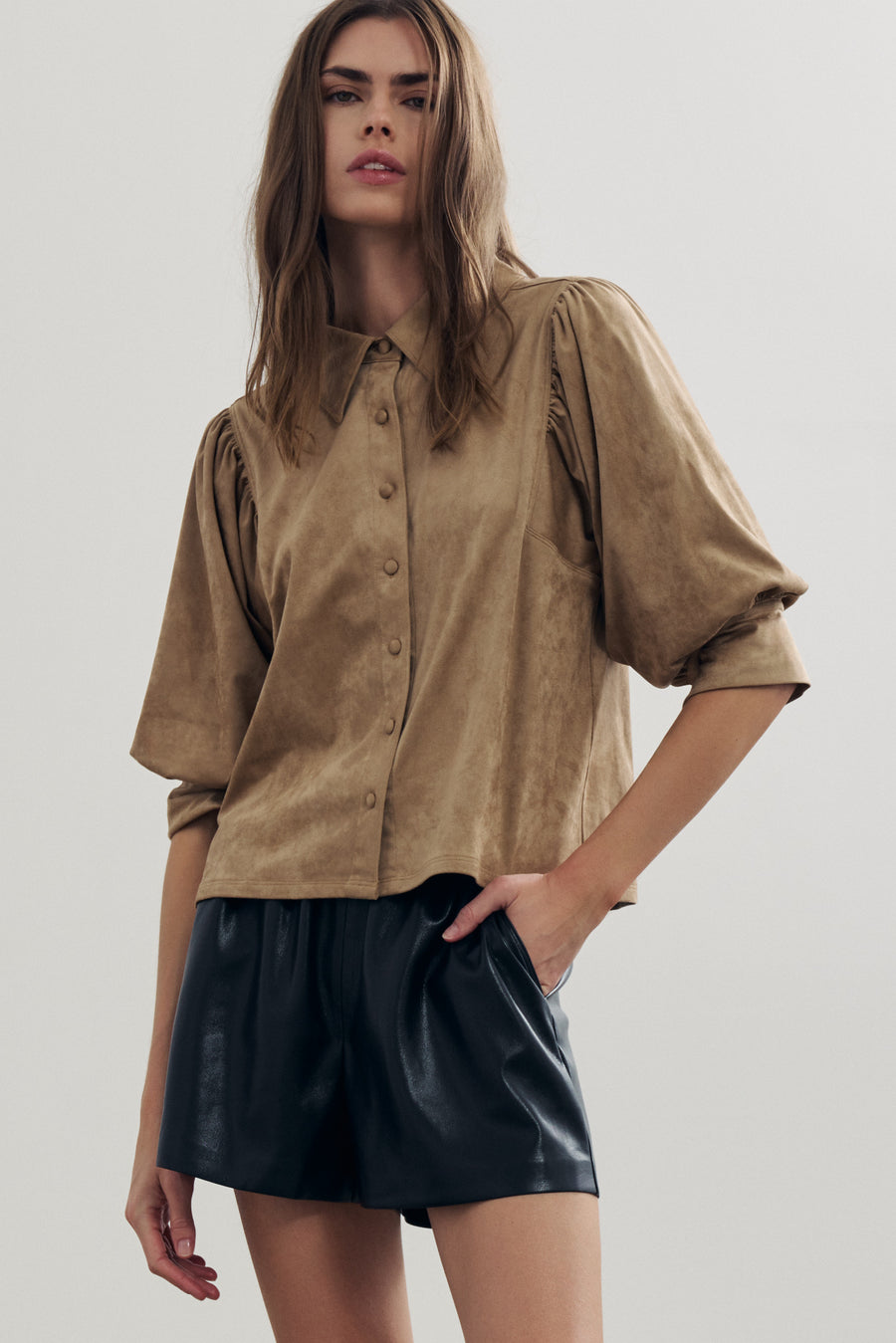 A woman modeling a cropped tan suede-like button-up blouse with voluminous short sleeves